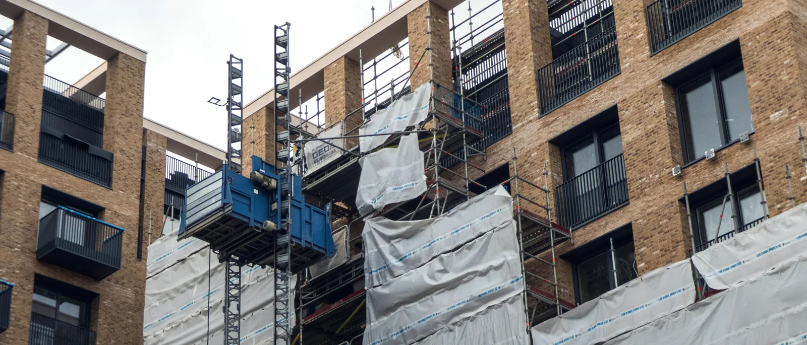 Construction site behind scaffolding, hoist and wrapped floors mid-build