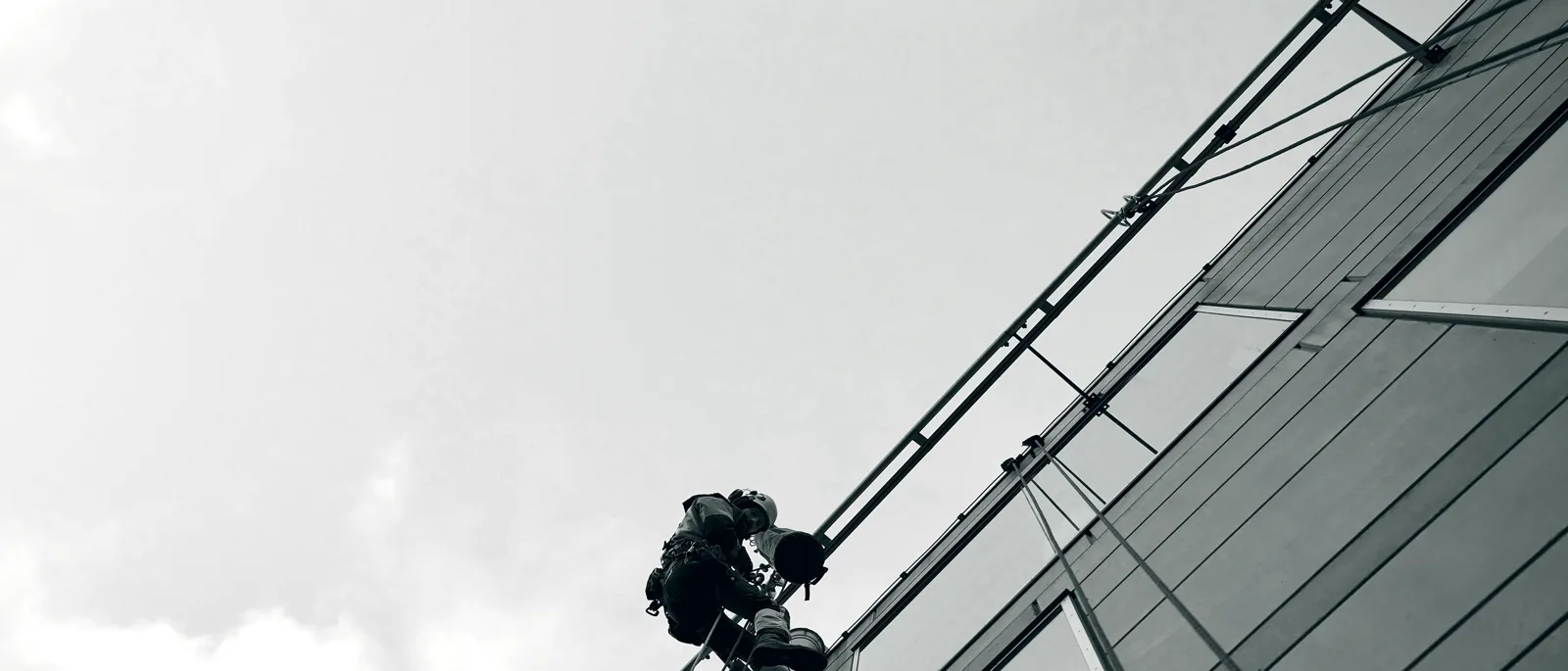 A rope-access technician working on ropes against a glass building facade